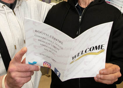 Picture of two people holding a welcome to the Booth Centre leaflet
